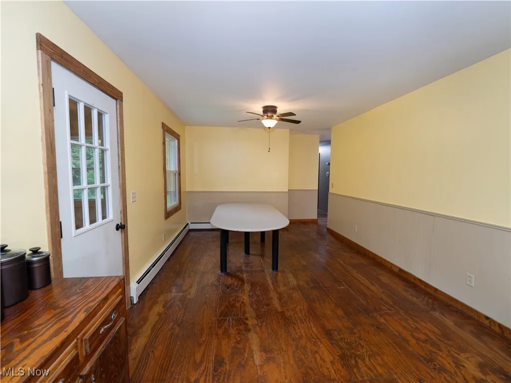 Unfurnished dining area with dark wood-style floors, a baseboard heating unit, and a ceiling fan