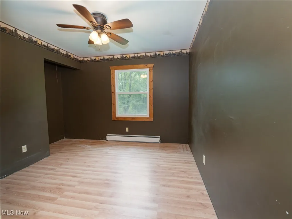 Empty room with light wood-style flooring, a baseboard radiator, and ceiling fan