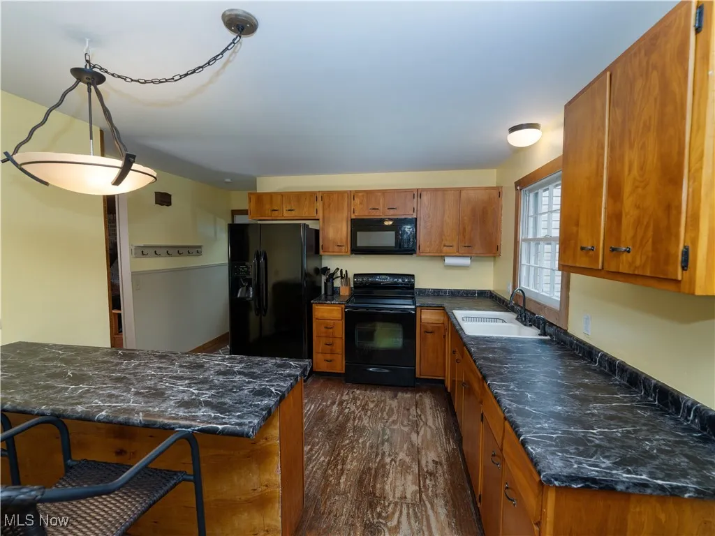 Kitchen featuring black appliances, brown cabinets, dark wood-type flooring, and dark stone counters