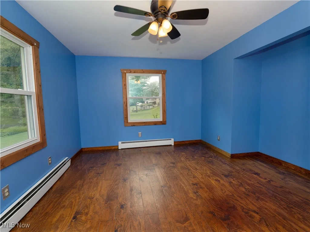 Unfurnished room featuring baseboard heating, dark wood-type flooring, and ceiling fan