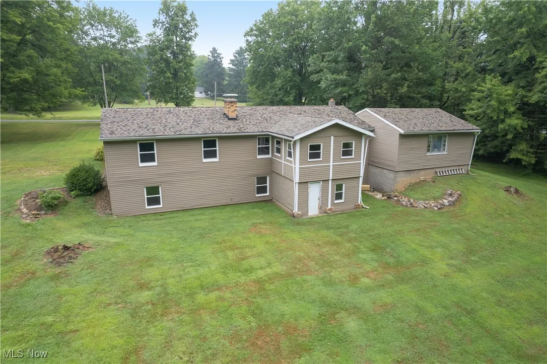 Back of house featuring a chimney, a lawn, and view of wooded area