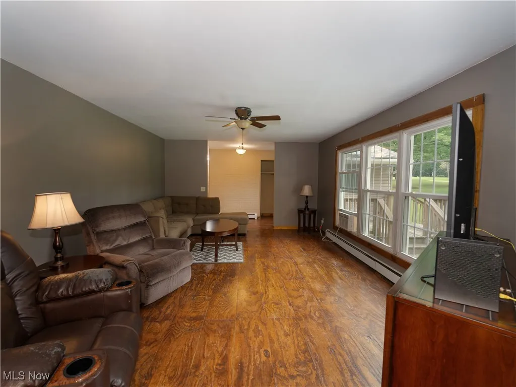 Living area featuring wood finished floors, baseboard heating, and ceiling fan