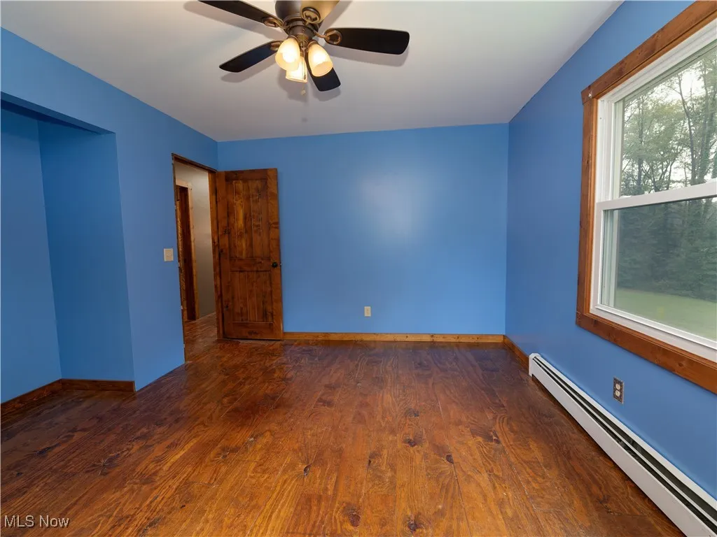 Unfurnished room featuring a baseboard heating unit, dark wood-style floors, and a ceiling fan