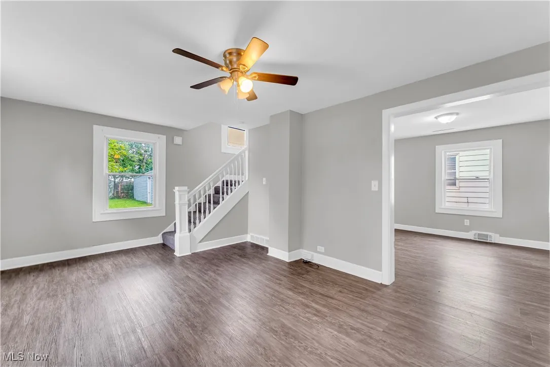 Unfurnished living room featuring dark wood-type flooring, stairs, and a ceiling fan
