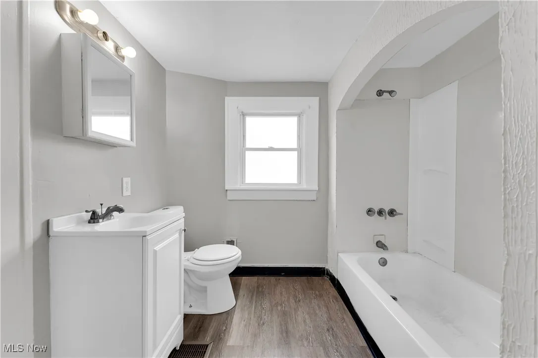 Full bath with shower / bathtub combination, vanity, and dark wood-style flooring