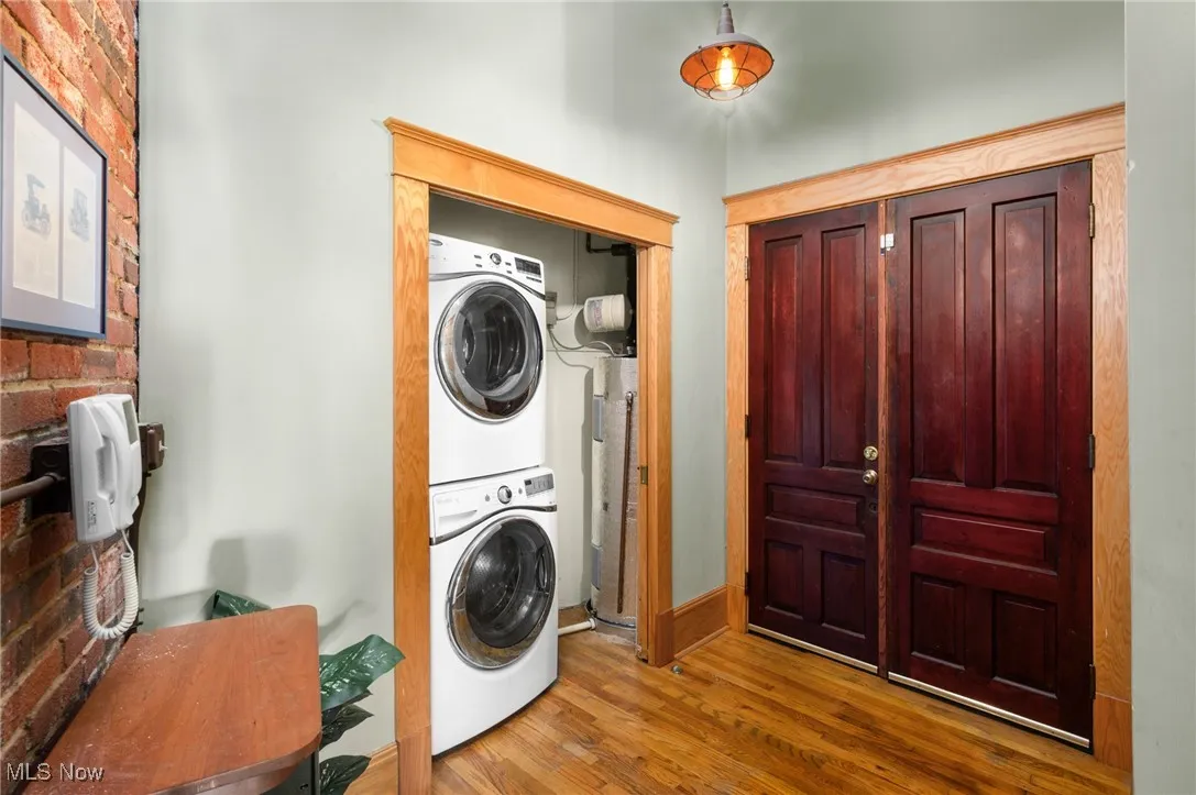 Laundry area with brick wall, wood finished floors, estacked washer and dryer, and water heater