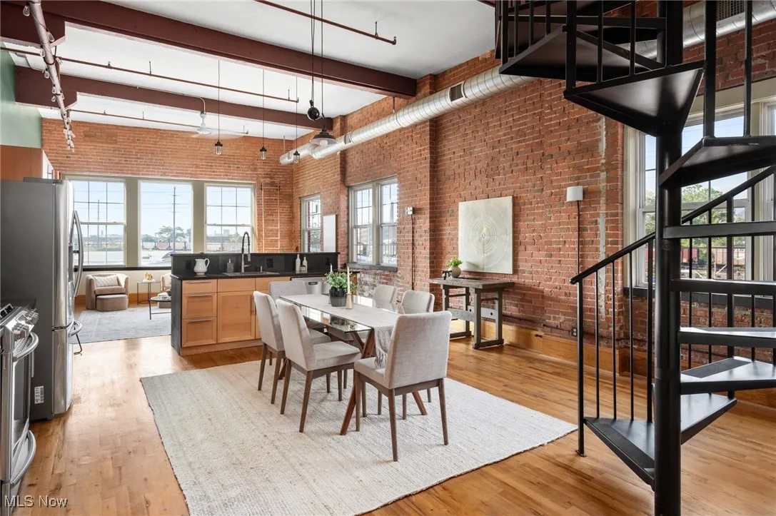 Dining space featuring brick wall, light wood-style floors, a high ceiling, stairway, and beam ceiling