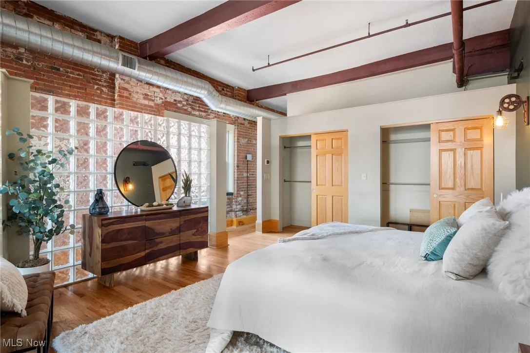 Bedroom with multiple closets, wood finished floors, beam ceiling, and brick wall