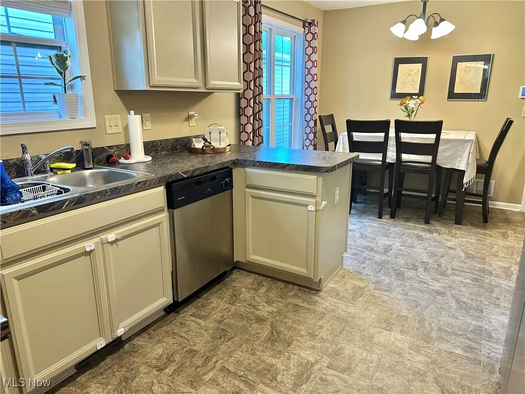 Kitchen featuring a peninsula, stainless steel dishwasher, dark countertops, and a chandelier