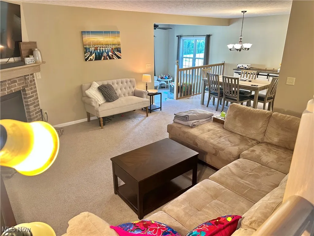 Carpeted living area featuring a textured ceiling, a brick fireplace, and a chandelier