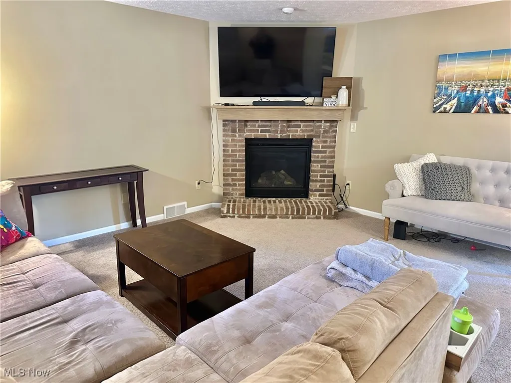 Living room featuring carpet floors, a fireplace, and a textured ceiling