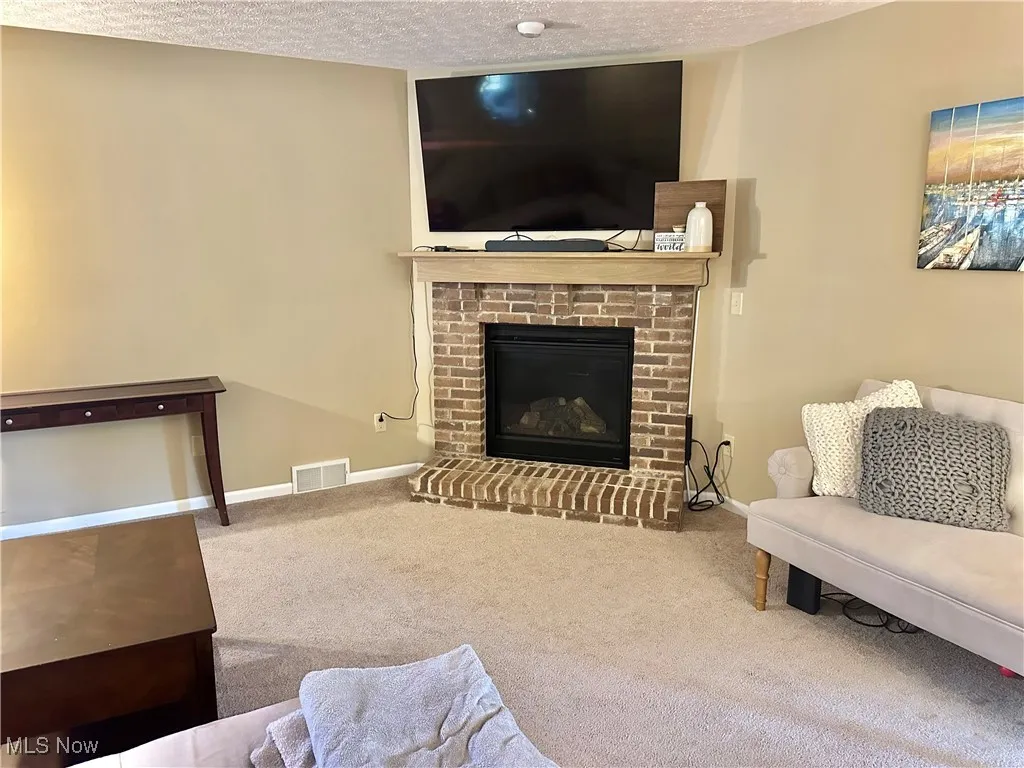 Living area with carpet, a brick fireplace, and a textured ceiling