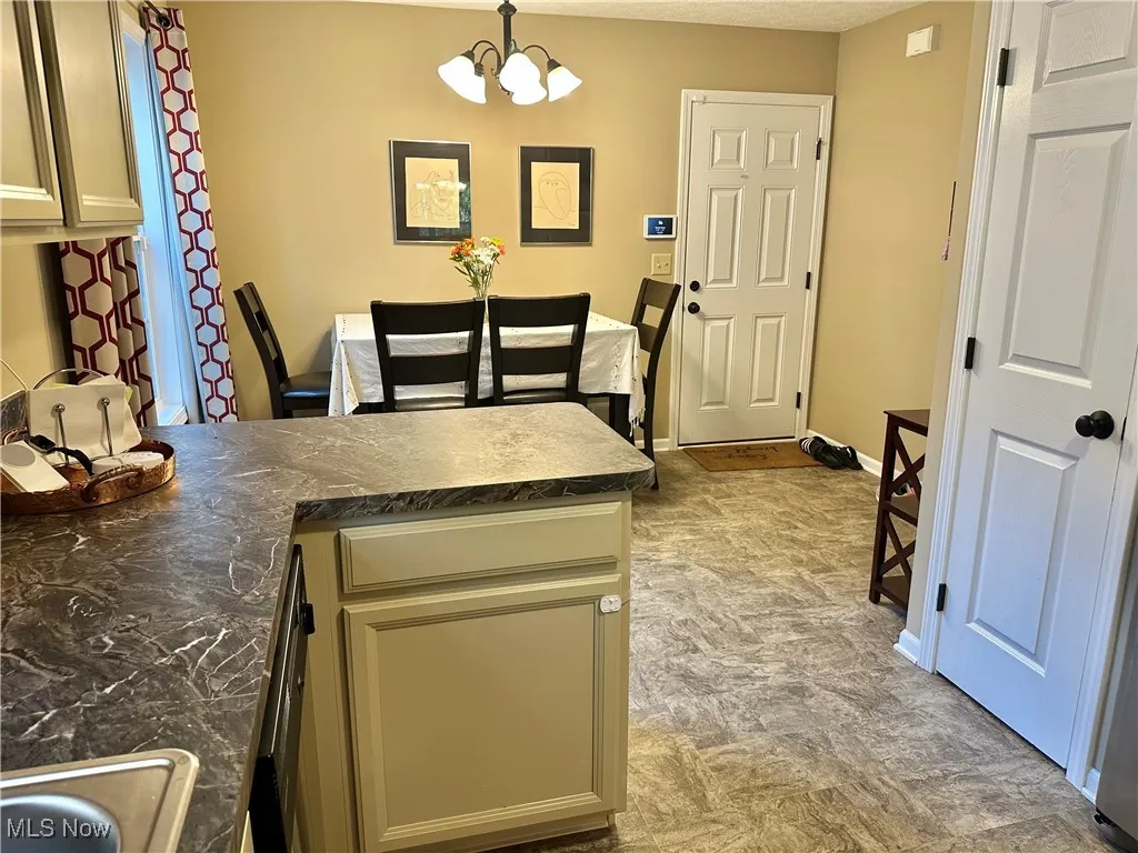 Kitchen featuring hanging light fixtures, a peninsula, dark countertops, a chandelier, and cream cabinets