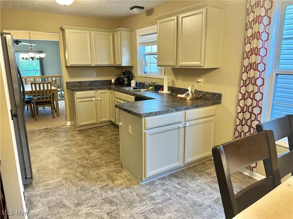 Kitchen featuring a peninsula, freestanding refrigerator, dark countertops, a textured ceiling, and white cabinetry