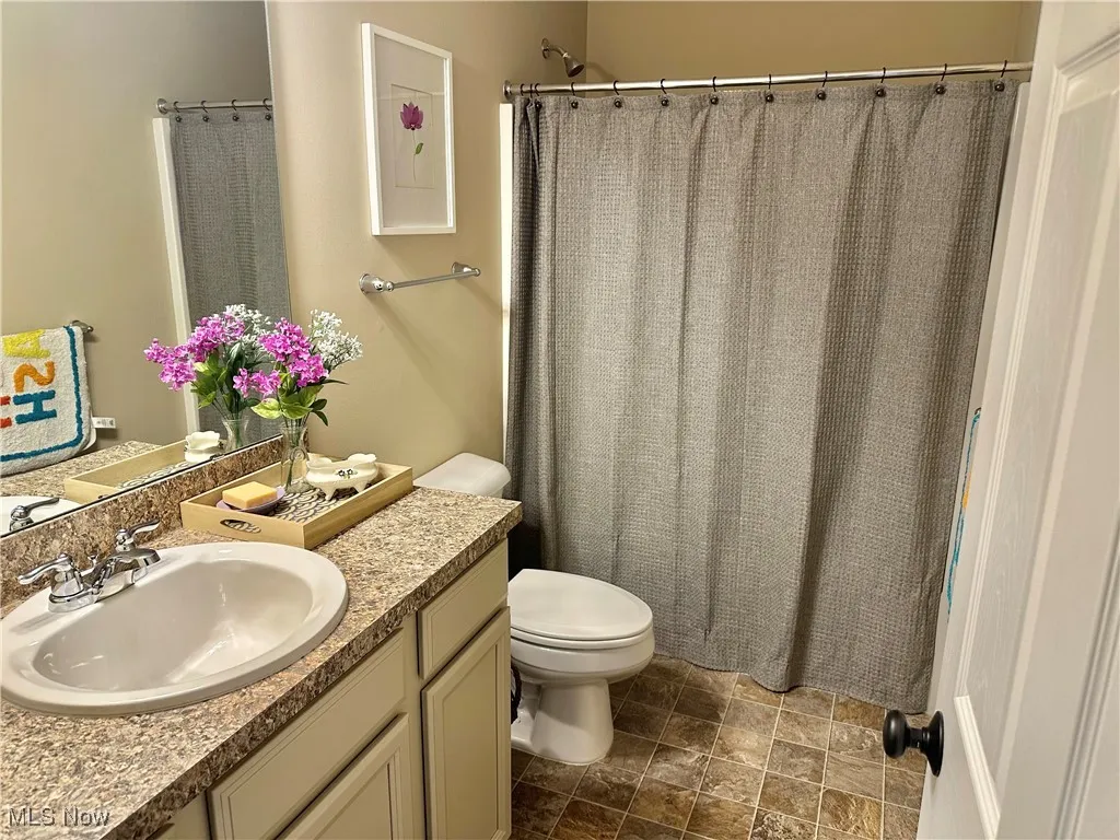 Full bathroom featuring vanity, curtained shower, and dark stone finish flooring