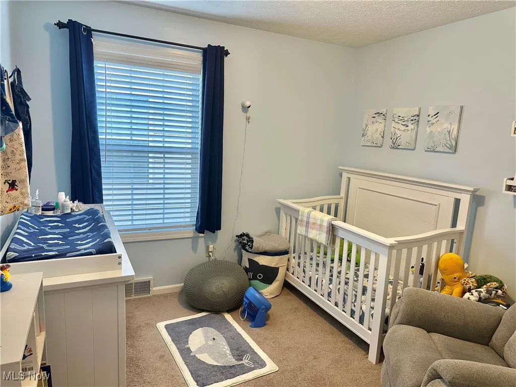 Bedroom with light colored carpet, a textured ceiling, and a crib