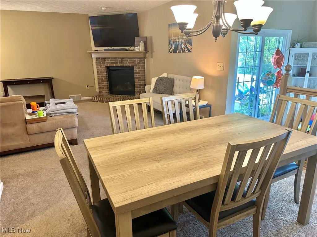 Dining space with carpet flooring, a chandelier, a fireplace, and a textured ceiling
