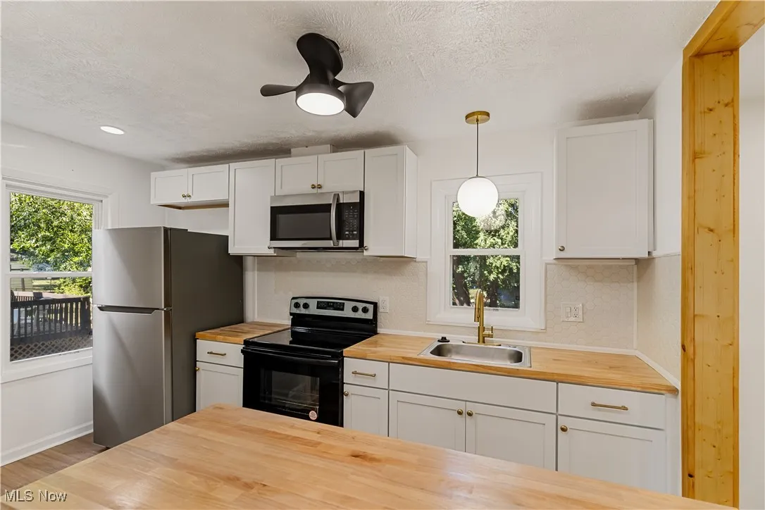 Kitchen with white cabinetry, stainless steel appliances, pendant lighting, a textured ceiling, and butcher block countertops