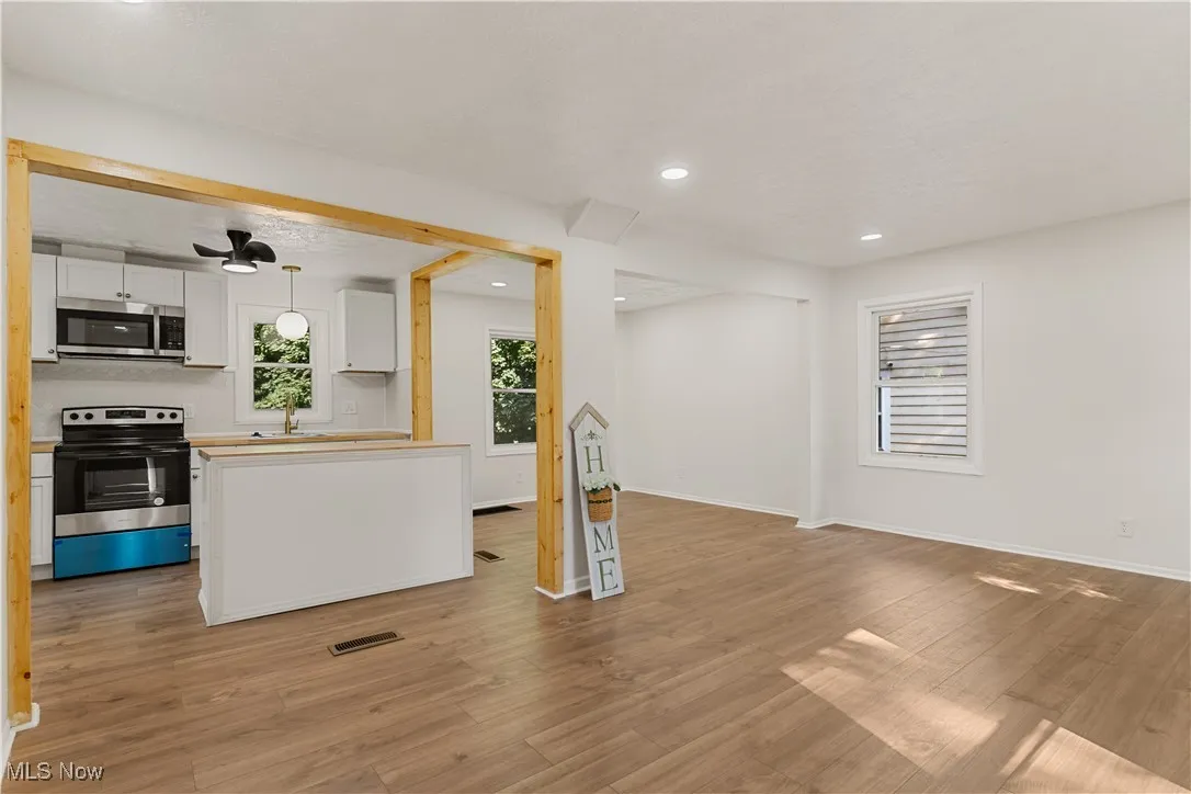 Kitchen with white cabinetry, appliances with stainless steel finishes, decorative light fixtures, light wood-type flooring, and open floor plan