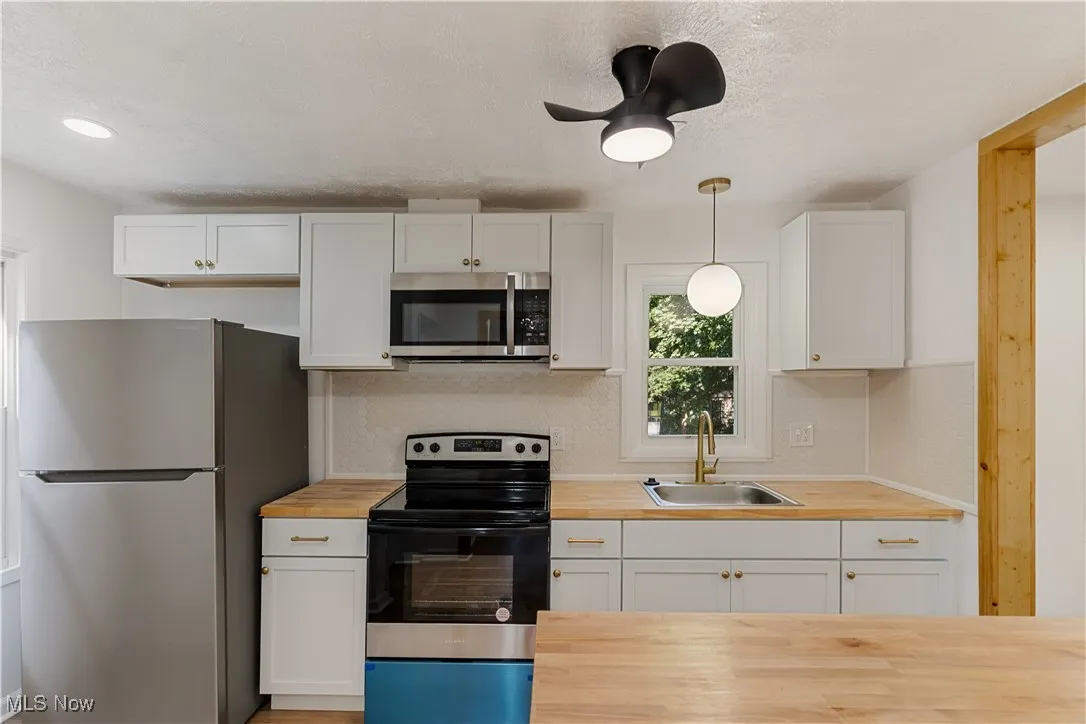 Kitchen with appliances with stainless steel finishes, white cabinets, pendant lighting, decorative backsplash, and a textured ceiling