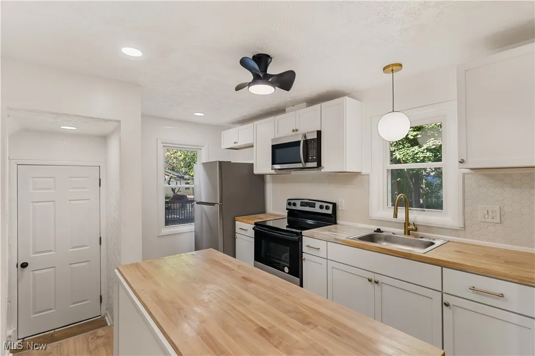 Kitchen featuring white cabinetry, appliances with stainless steel finishes, butcher block counters, decorative light fixtures, and backsplash