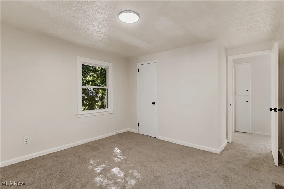 Carpeted empty room with a textured ceiling and baseboards