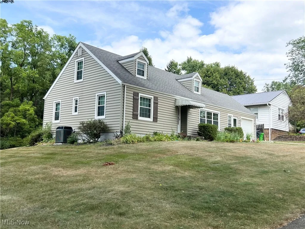 Cape cod house featuring an attached garage, a front lawn, and a shingled roof