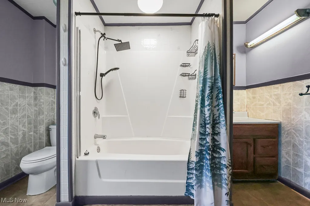 Bathroom with tile walls, a wainscoted wall, shower / bathtub combination with curtain, ornamental molding, and vanity