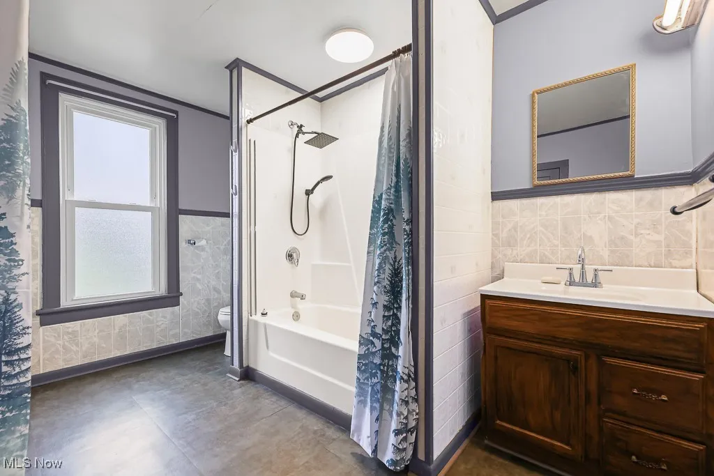 Bathroom with shower / bath combo with shower curtain, tile walls, vanity, and a wainscoted wall