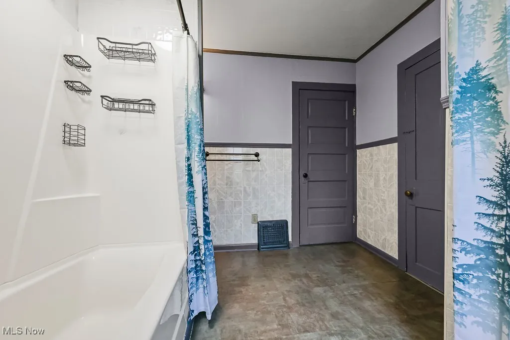 Full bath featuring tile walls, wainscoting, ornamental molding, and shower / bath combo