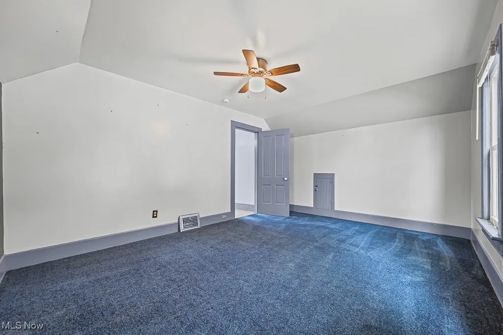 Bedroom with dark colored carpet, lofted ceiling, and ceiling fan