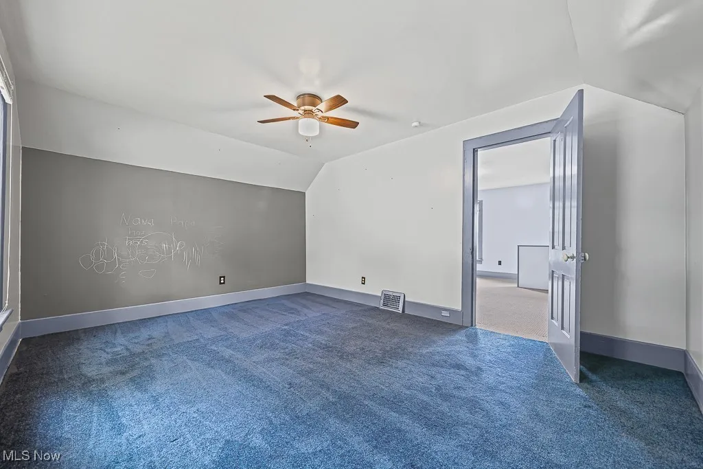 Bedroom with dark colored carpet, vaulted ceiling, and ceiling fan
