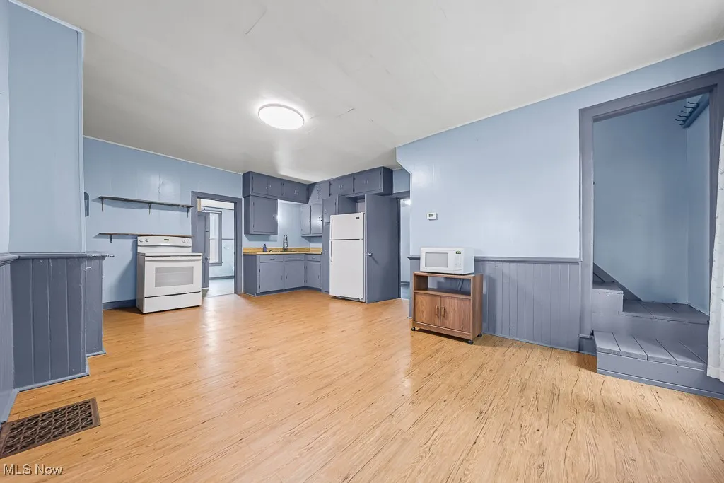 Kitchen featuring light wood finished floors, white appliances, blue cabinets, a wainscoted wall, and light countertops