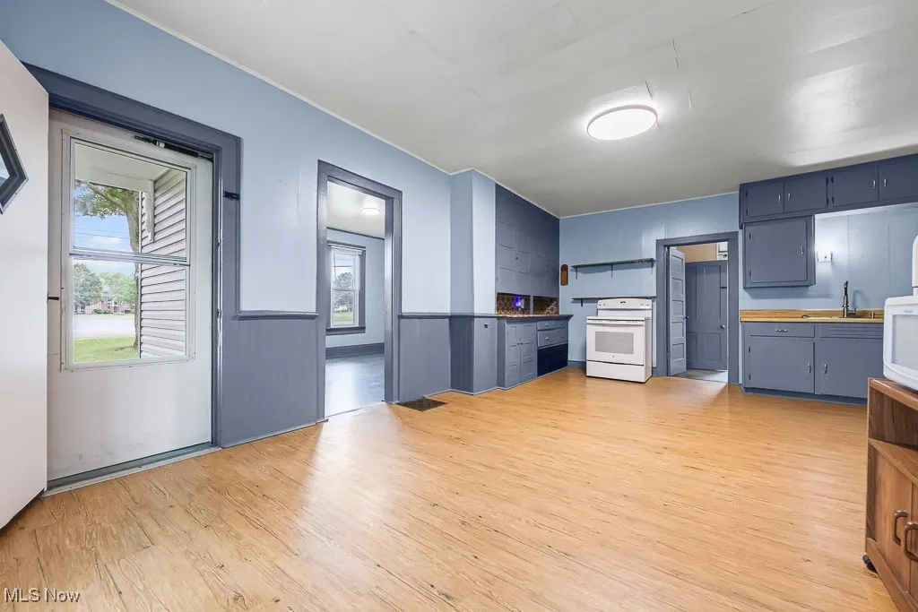 Kitchen featuring light wood-style flooring, open shelves, white appliances, blue cabinets, and a wainscoted wall