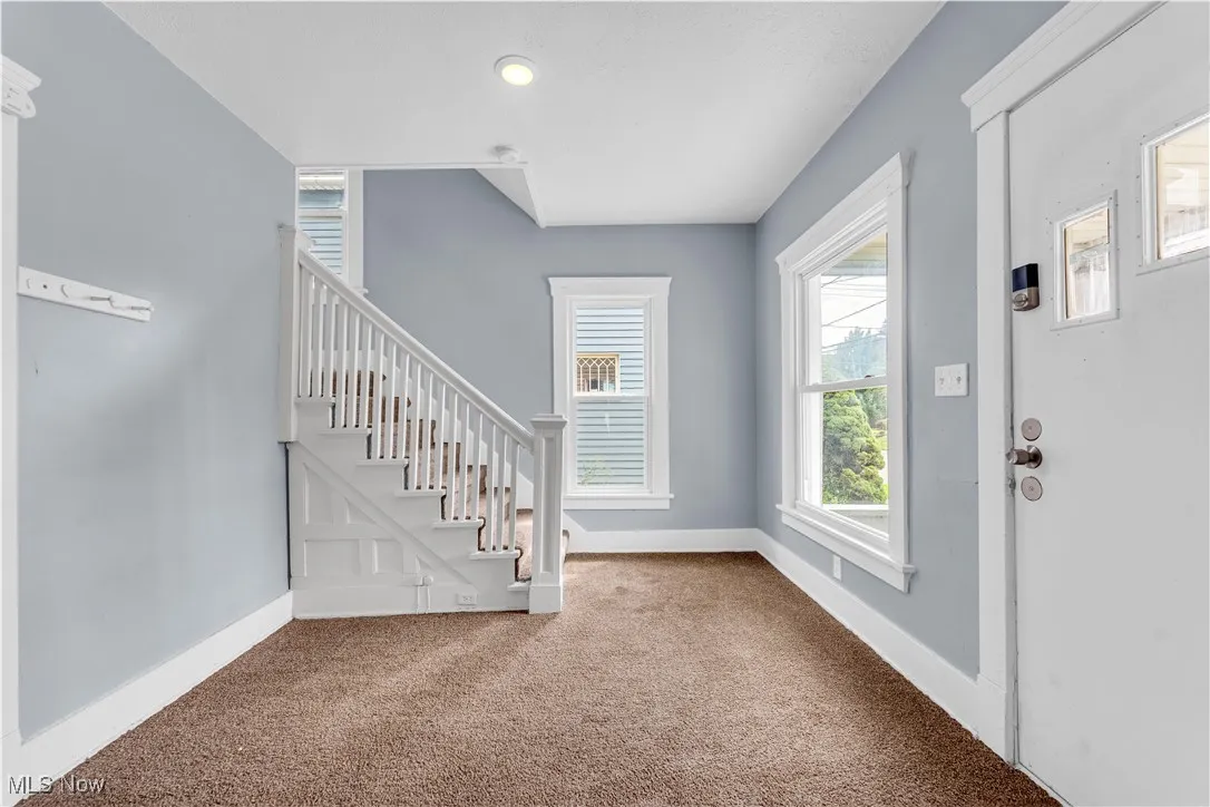 Carpeted entryway featuring stairway and baseboards