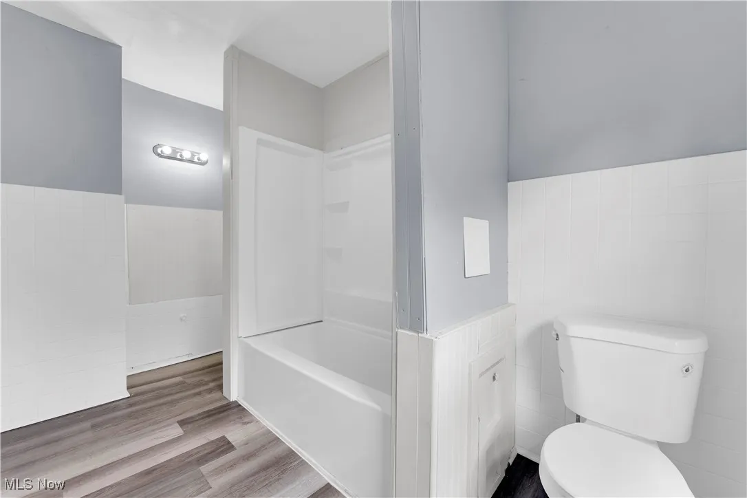 Full bath featuring tile walls, wainscoting, wood finished floors, and tub / shower combination