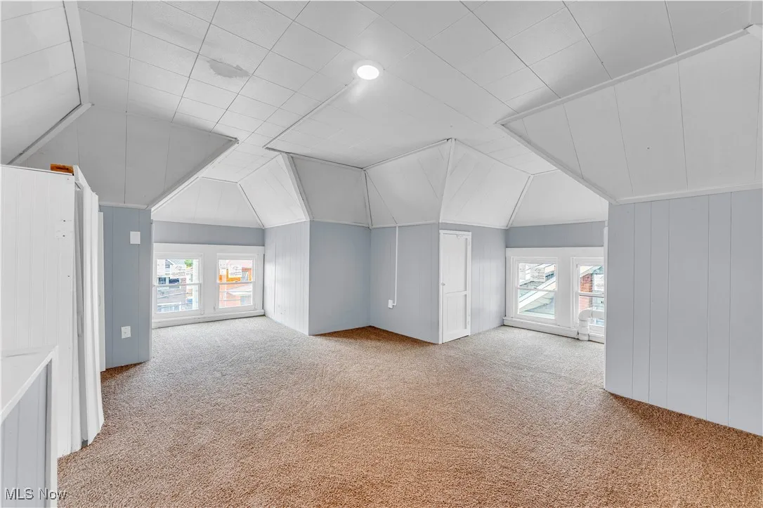 Additional living space featuring light colored carpet, vaulted ceiling, and wooden walls