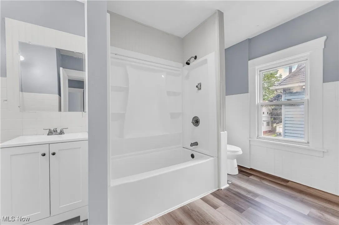 Bathroom featuring light wood-style floors, bathing tub / shower combination, vanity, wainscoting, and tile walls
