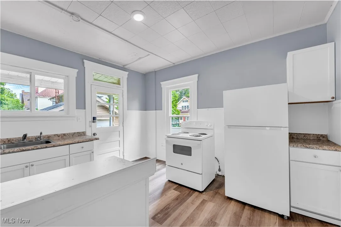 Kitchen featuring white cabinets, white appliances, light wood-style floors, and light stone counters