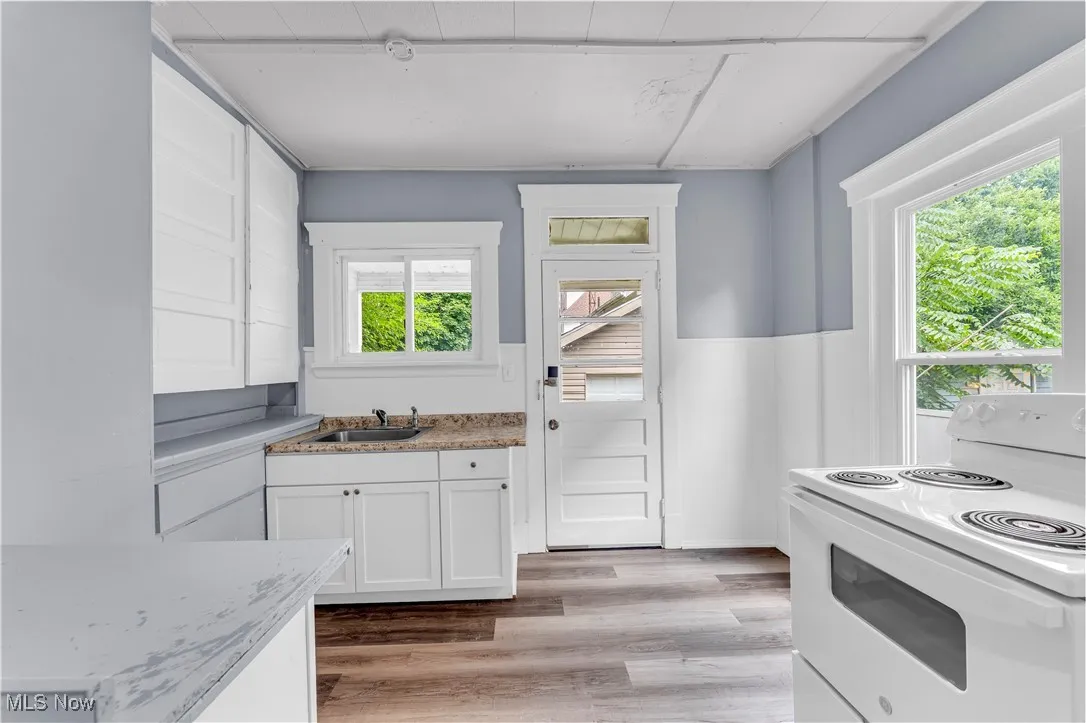 Kitchen featuring electric range, white cabinetry, light wood-style flooring, and light stone counters