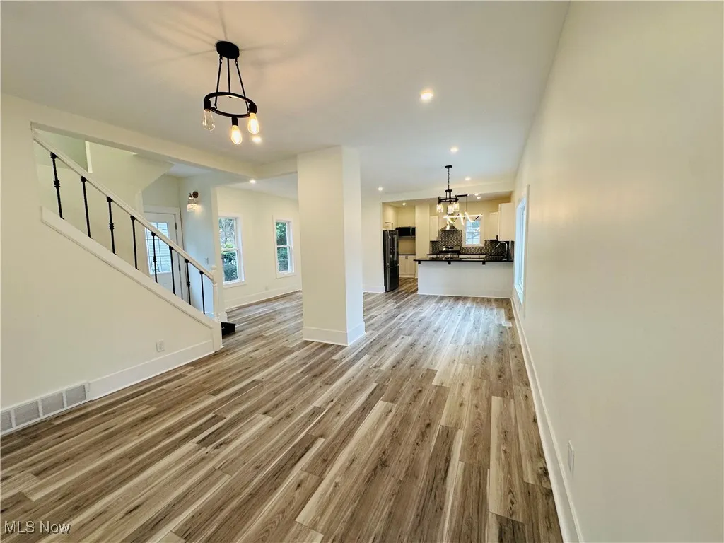 Unfurnished living room with stairway, a chandelier, light wood finished floors, and recessed lighting