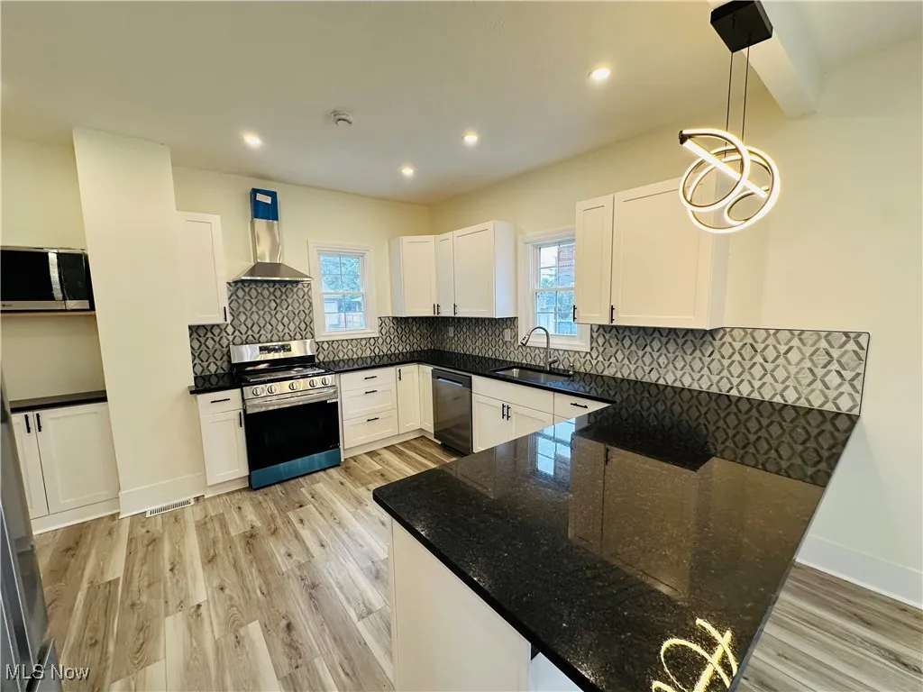 Kitchen featuring backsplash, stainless steel appliances, dark stone counters, light wood finished floors, and recessed lighting