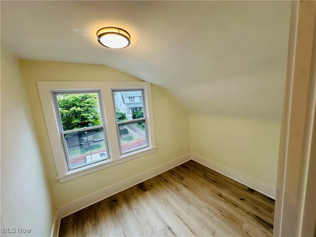 Additional living space with light wood-style flooring and vaulted ceiling