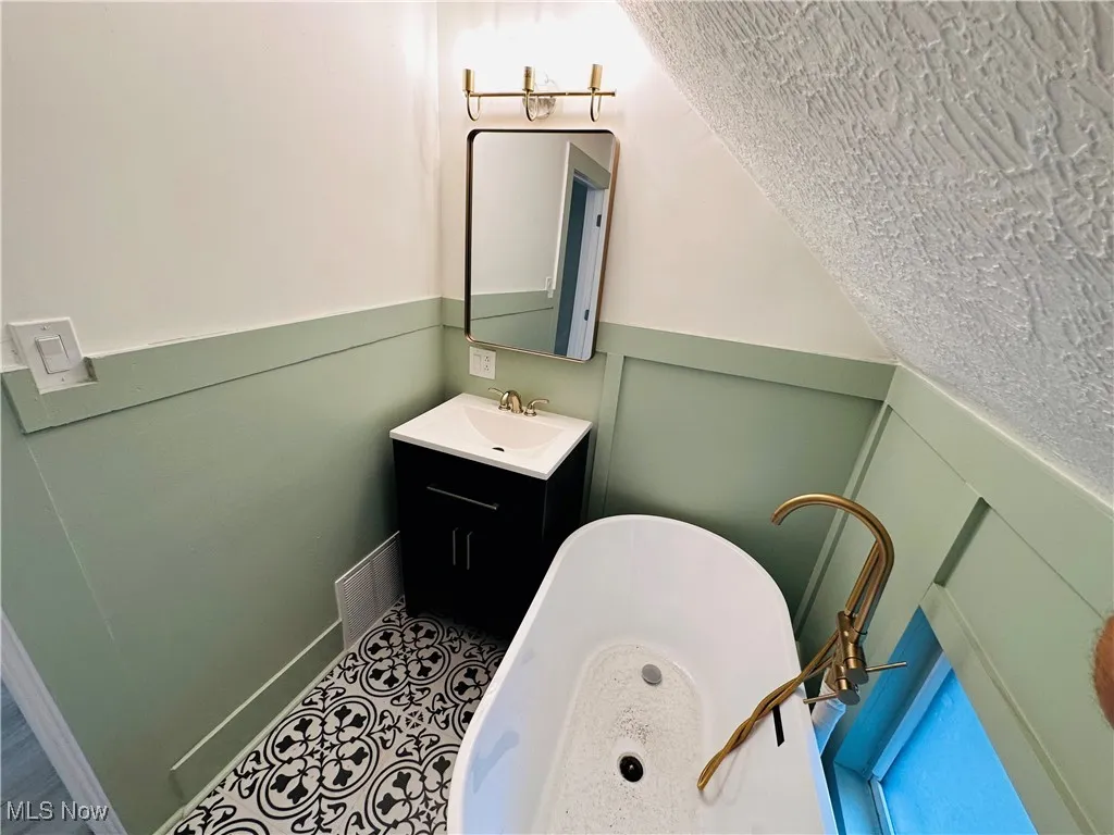 Bathroom with a freestanding bath, vanity, a textured ceiling, tile patterned floors, and lofted ceiling