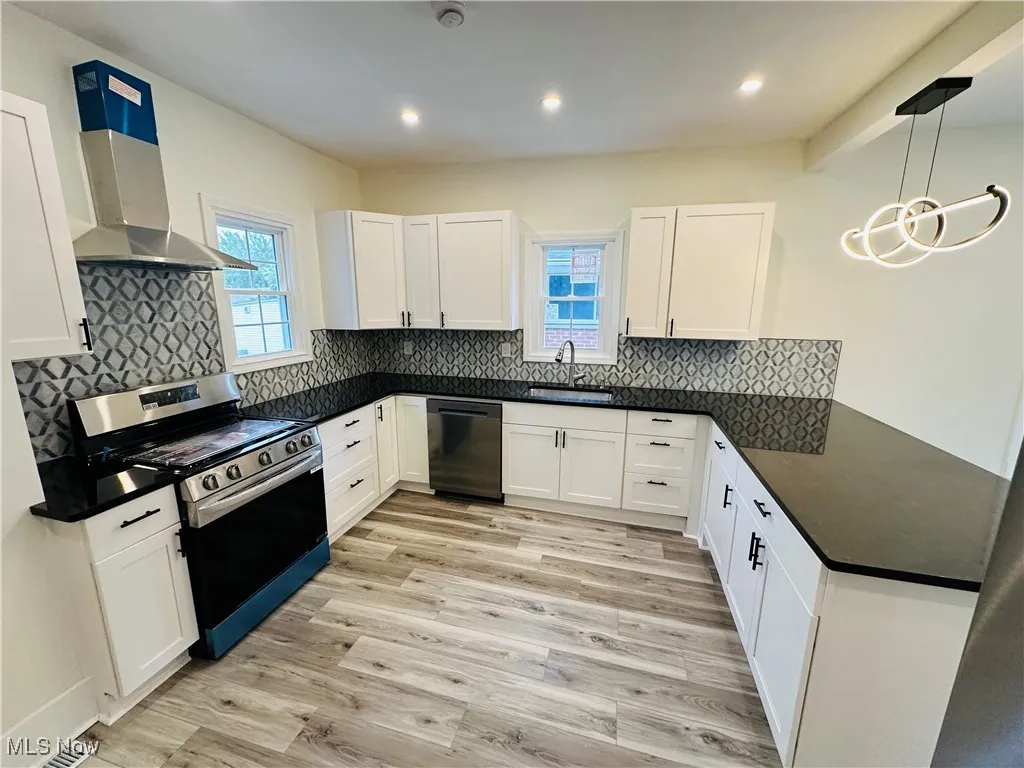 Kitchen with stainless steel range oven, white cabinetry, wall chimney range hood, recessed lighting, and beam ceiling
