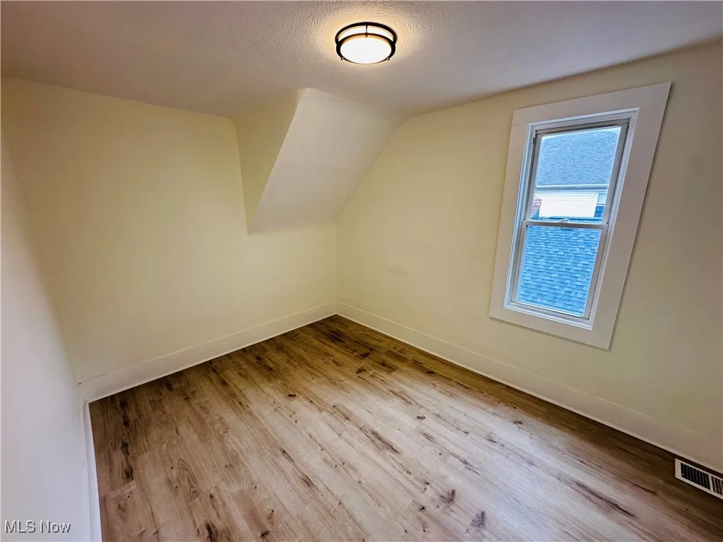 Bonus room featuring light wood-type flooring, a textured ceiling, and vaulted ceiling