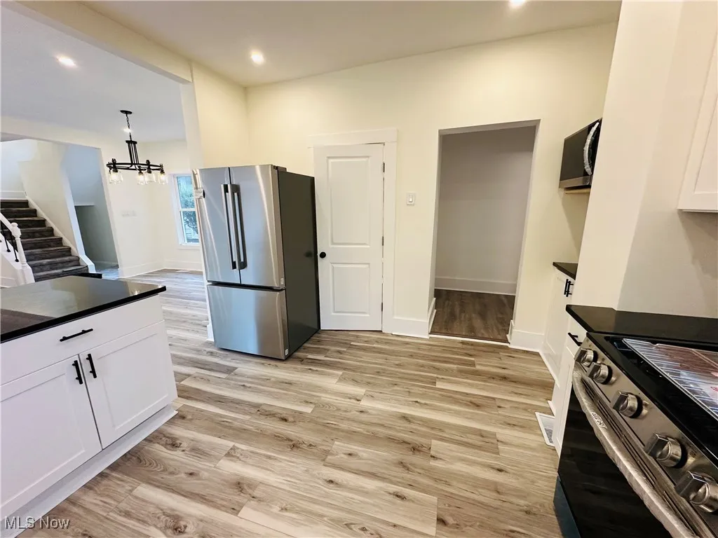 Kitchen with appliances with stainless steel finishes, light wood finished floors, white cabinetry, recessed lighting, and a chandelier