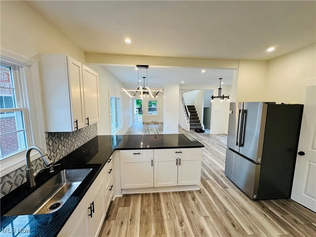 Kitchen with a chandelier, freestanding refrigerator, decorative backsplash, a peninsula, and light wood-type flooring