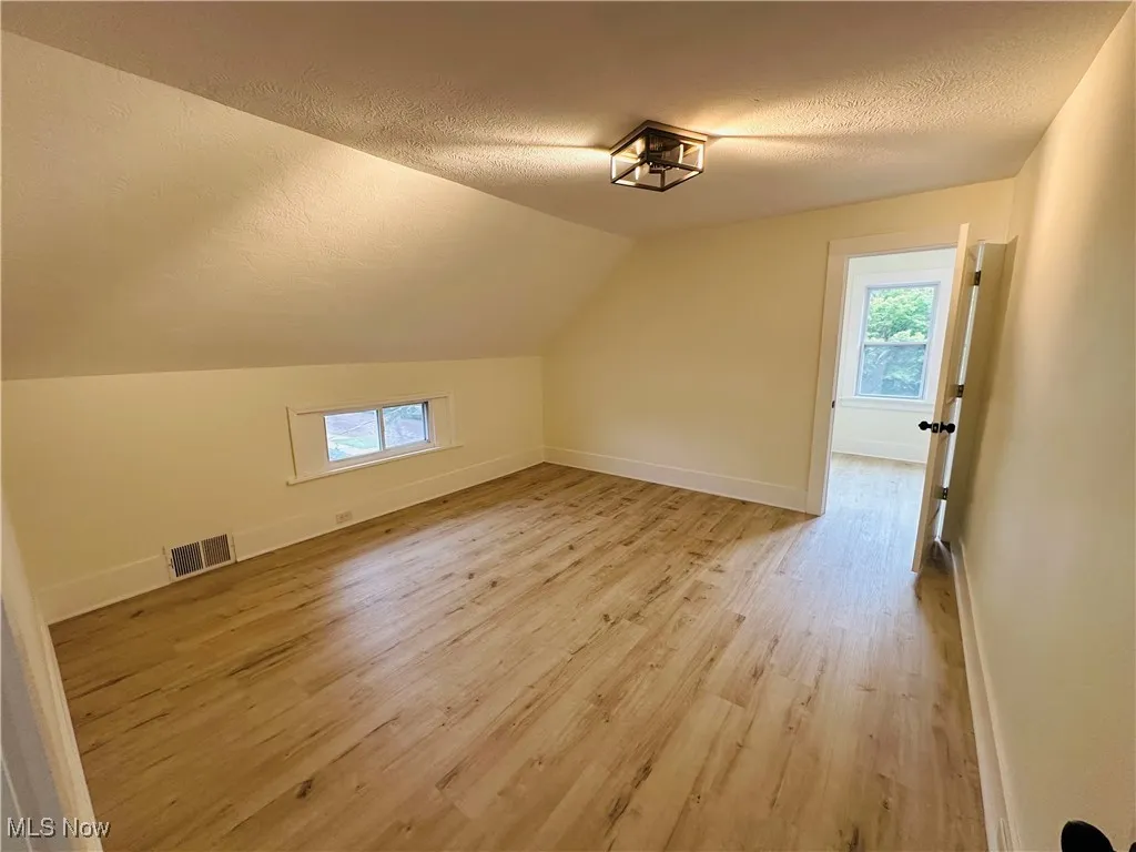 Additional living space with a textured ceiling, vaulted ceiling, healthy amount of natural light, and light wood-type flooring