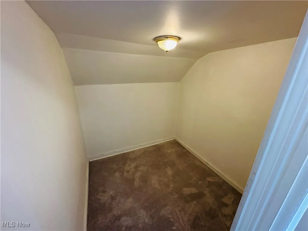 Bonus room with dark colored carpet and vaulted ceiling